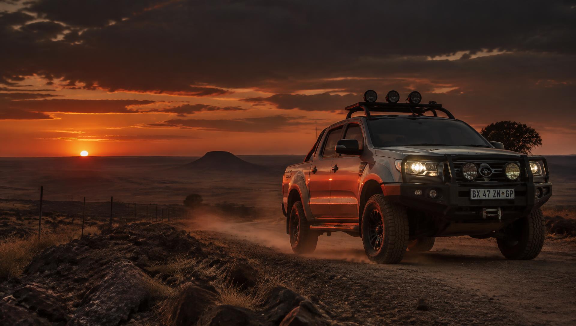 Bakkie with bull bar and spotlights on a dirt road at sunset